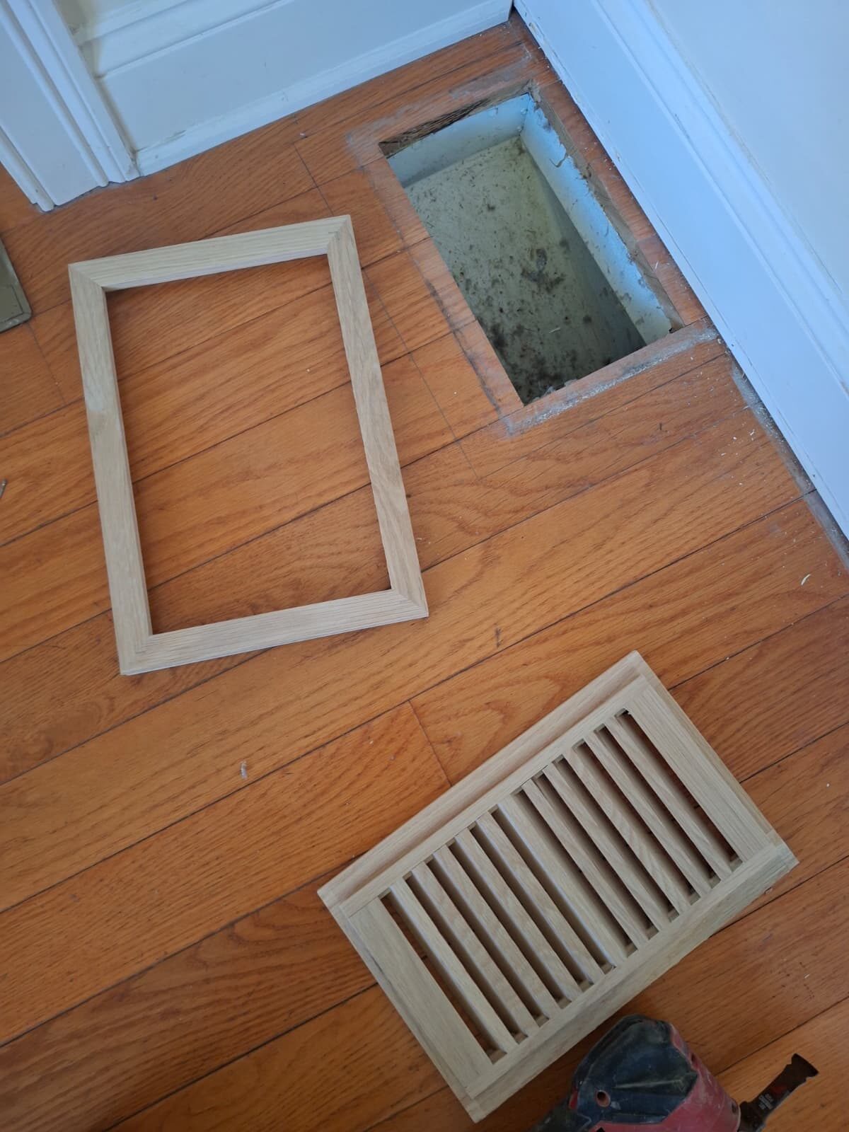 Oak floor vent frame and grille prepared next to a hardwood floor opening — before install