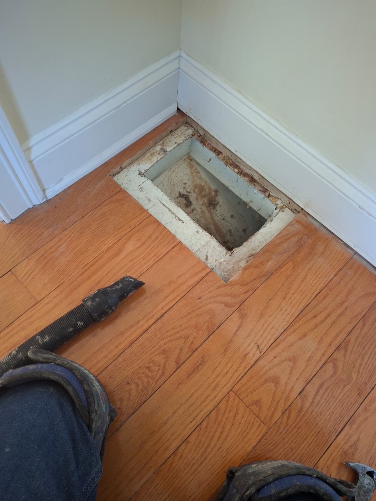 Bare floor vent opening cleaned out in hardwood flooring at baseboard corner during prep